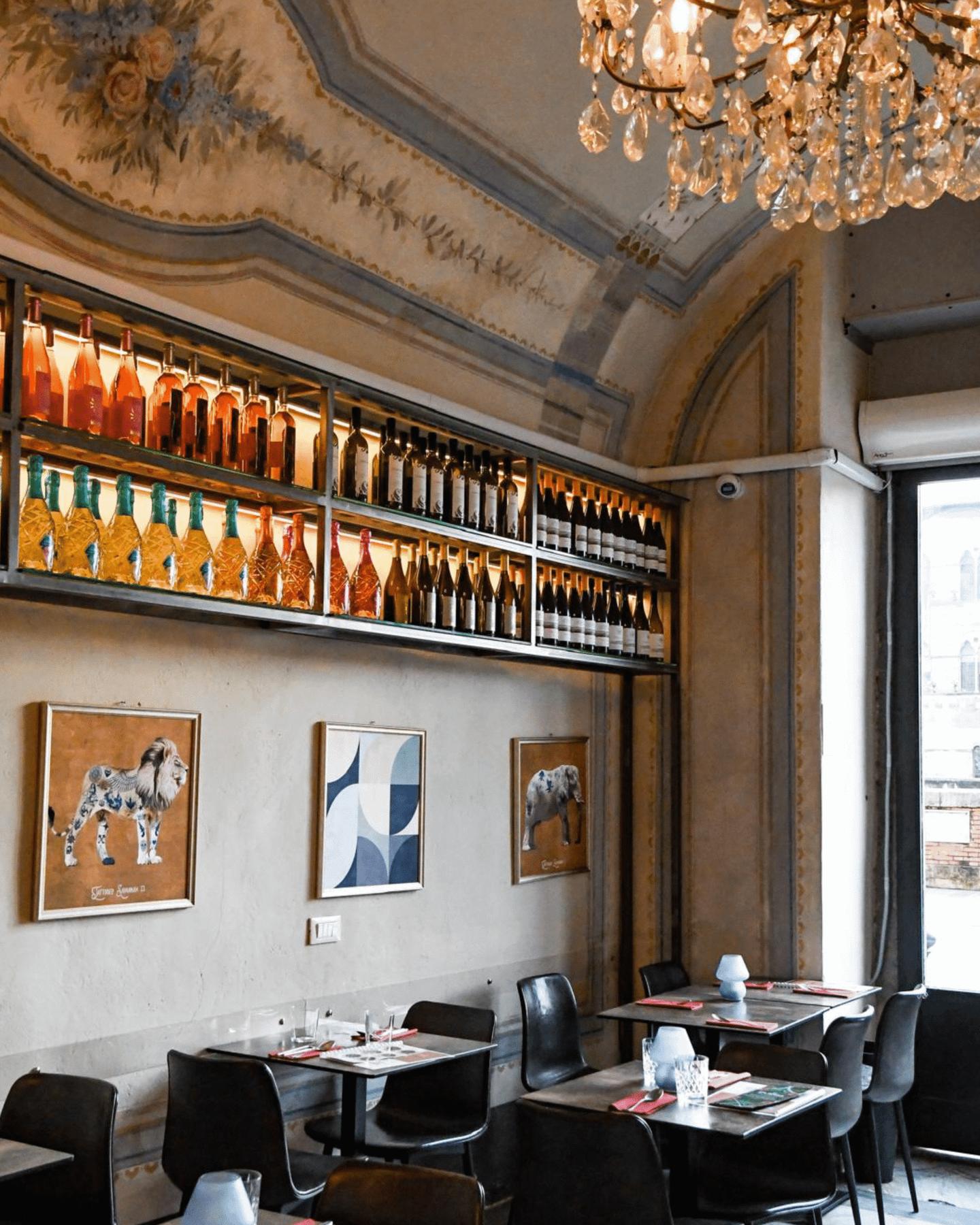 La sala di Misù: lampadario di cristallo, soffitto affrescato, parete di bottiglie retroilluminata e tavoli scuri
