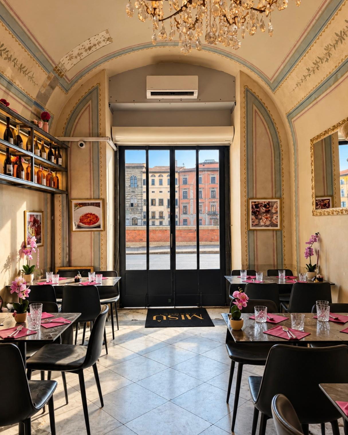 La sala di Misù di giorno: la volta affrescata, il lampadario di cristallo, i tavoli con i tovaglioli rosa e, oltre la porta a vetri, i palazzi del Lungarno